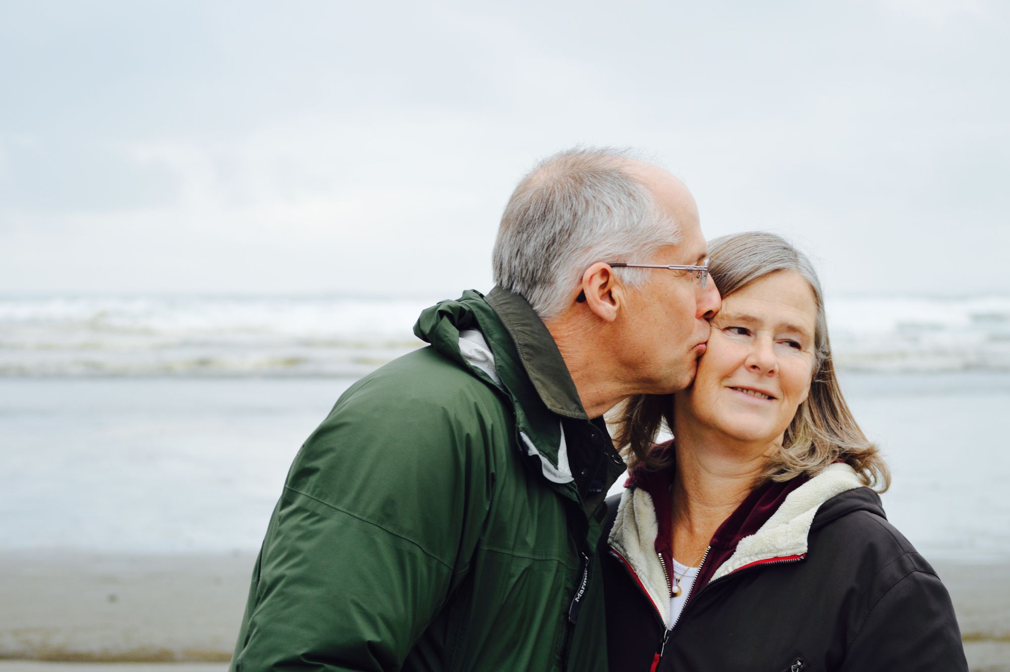Man kissing his wife on the cheek at the beach, symbolizing the importance of maintaining prostate health for life's precious moments, as guided by Overflow Health.